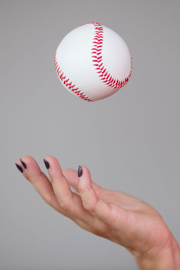 Daniela ist Deine Human Design Sparringspartnerin, die Dir die Bälle zuwirft. Das Foto zeigt Ihre Hand im Detail, während Sie einen Baseball hochwirft.